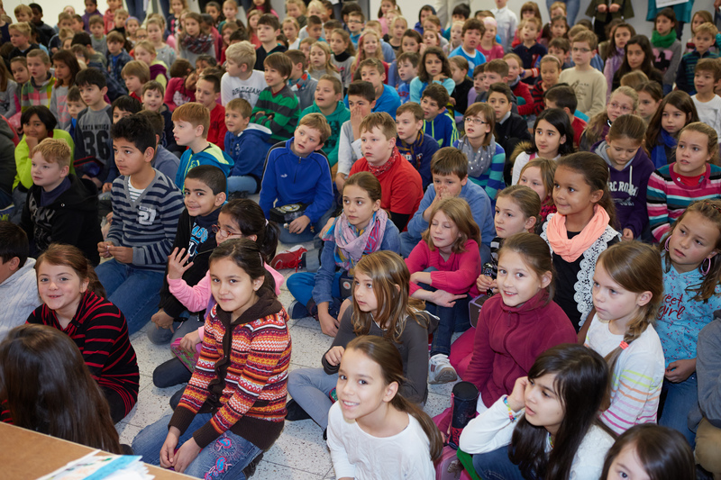 Schülerinnen und Schüler einer Grundschule sitzenn in der Aula