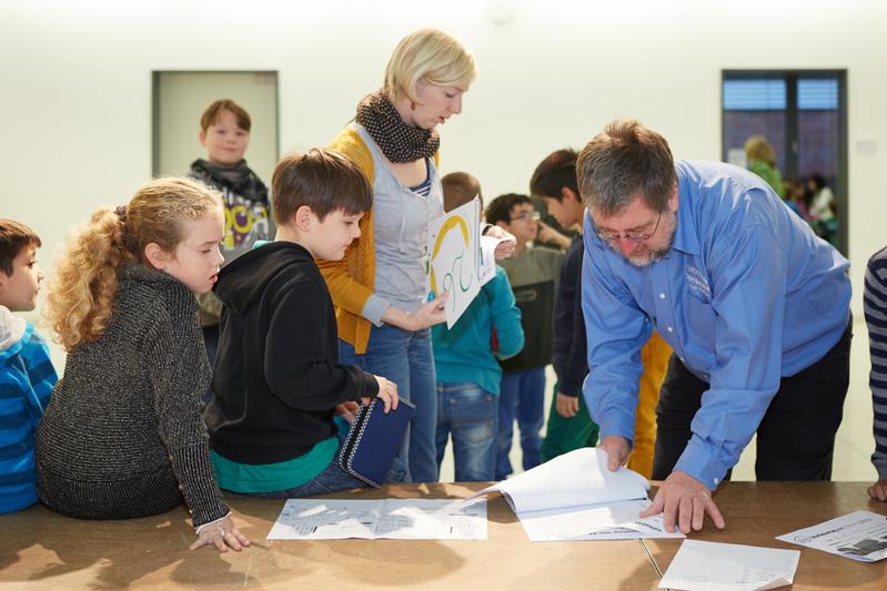 Lehrerin, Lehrer, Schülerinnen und Schüler beugen sich über ein Pult