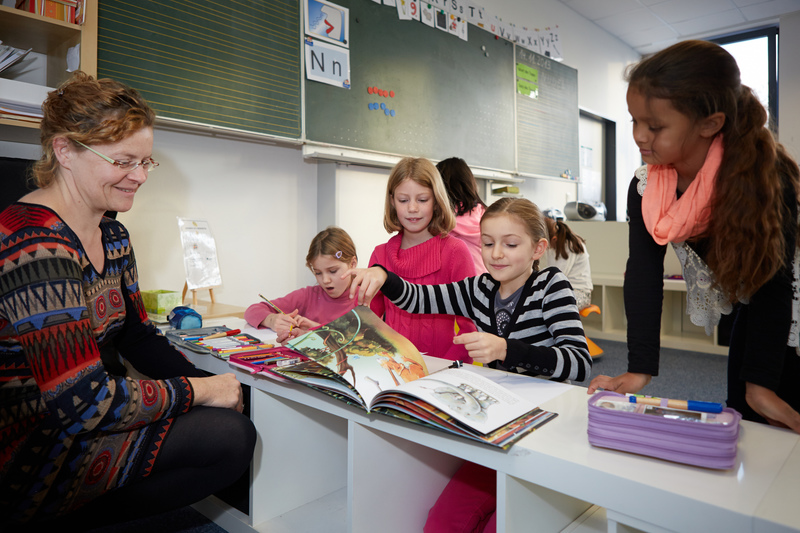 Lehrerin und Schülerinnen betrachten ein Buch