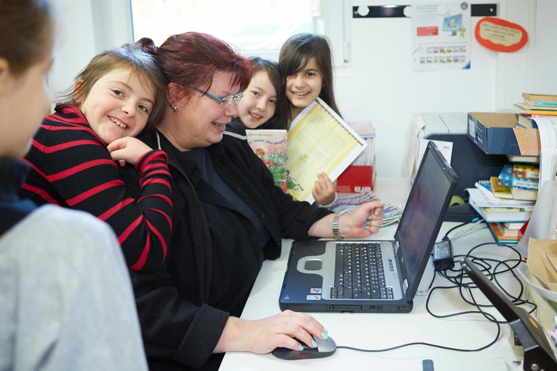 Schülerinnen und Schüler mit einer Erzieherin am Notebook