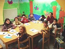 Blick in ein modernes Klassenzimmer mit Schülerinnen und Schülern und einer Lehrerin vor einer bunten Wand.