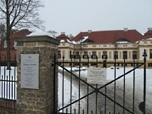 Blick durch einen hohen Zaun auf ein Schloss.
