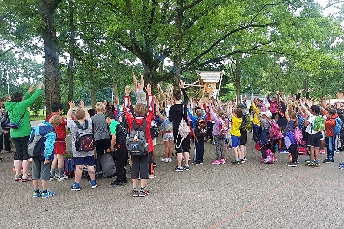 Schülerinnen und Schüler recken auf dem Schulhof die Arme hoch