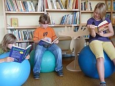 Drei Kinder sitzen oder liegen lesend auf Gymnastikbällen