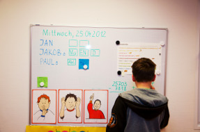 Ein Junge steht vor einer Magnetwand mit Bildern und Text.