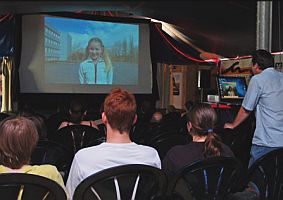 Zuschauer sitzen in einem abgedunkelten Raum vor einer Leinwand, auf der ein Film läuft.