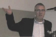 Foto eines Mannes, der gestikulierend am Rednerpult steht und spricht.