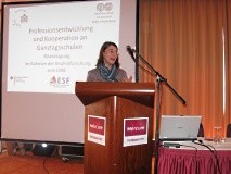 Eine Frau steht an einem Rednerpult vor einer Leinwand und spricht.