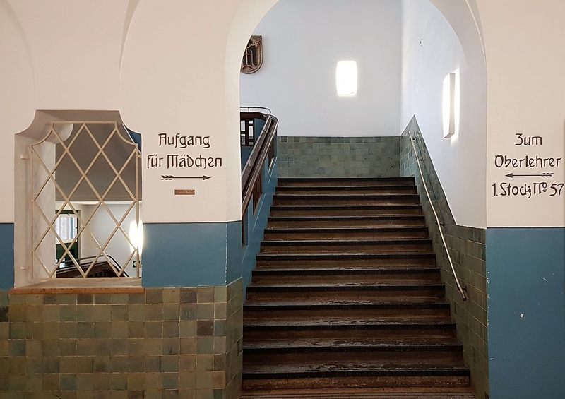 Treppenaufgang mit alter Beschriftung: "Aufgang für Mädchen" und "Zum Oberlehrer"