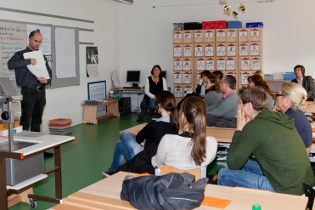 Erwachsene sitzen in einem Klassenraum, ein Lehrer erklärt etwas.